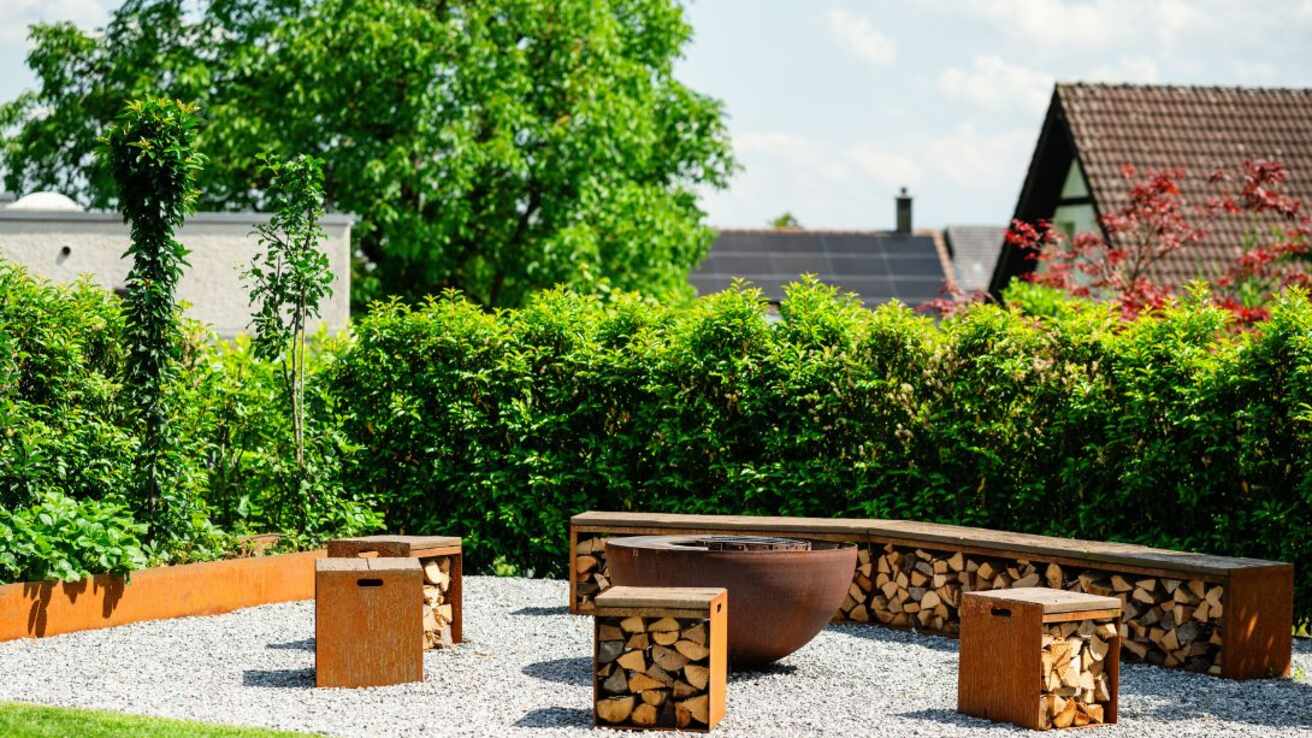 Gemütliche Gartenecke nach Gartenumbau mit Feuerstelle und rustikalen Holzhockern im Spätsommer