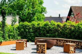 Gemütliche Gartenecke nach Gartenumbau mit Feuerstelle und rustikalen Holzhockern im Spätsommer